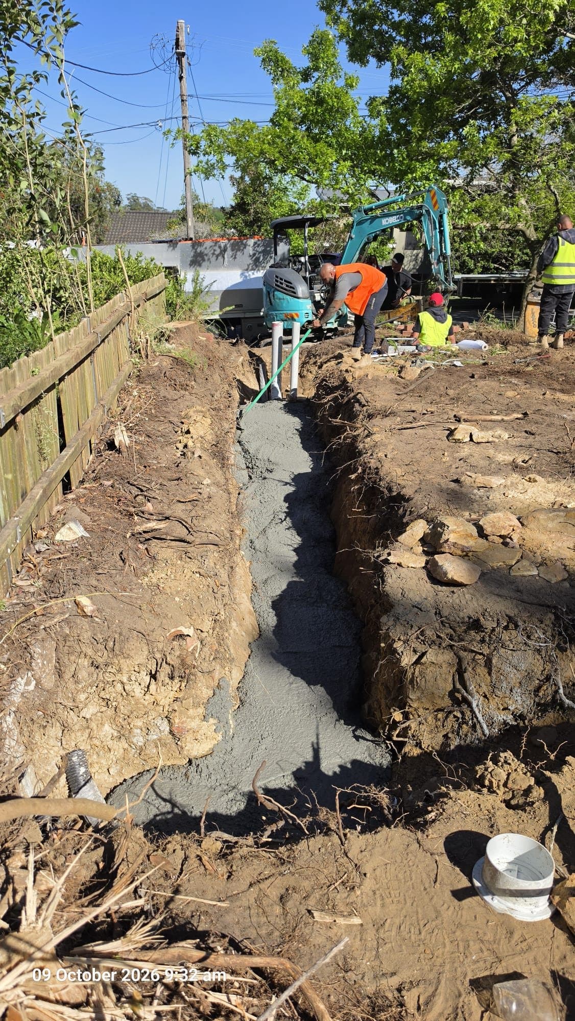 Concrete poured along a trench to encase new sewer pipework, with connection risers standing above it