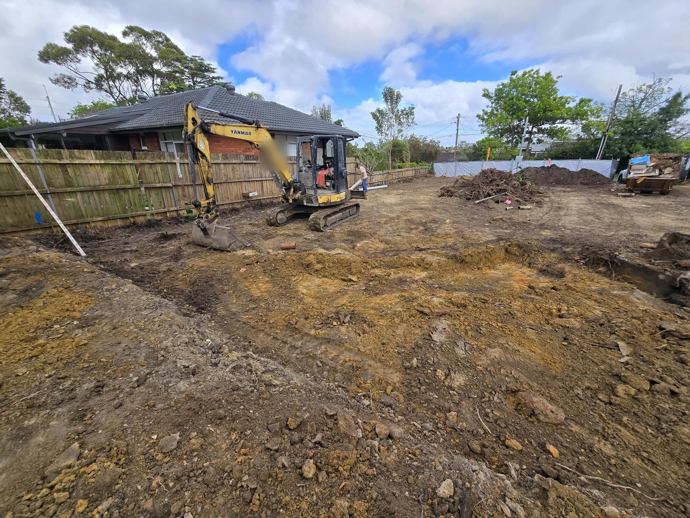 An excavator working on bulk excavation beside the boundary fence